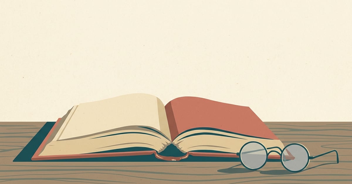 An open hardcover book on a desk beside a pair of reading glasses